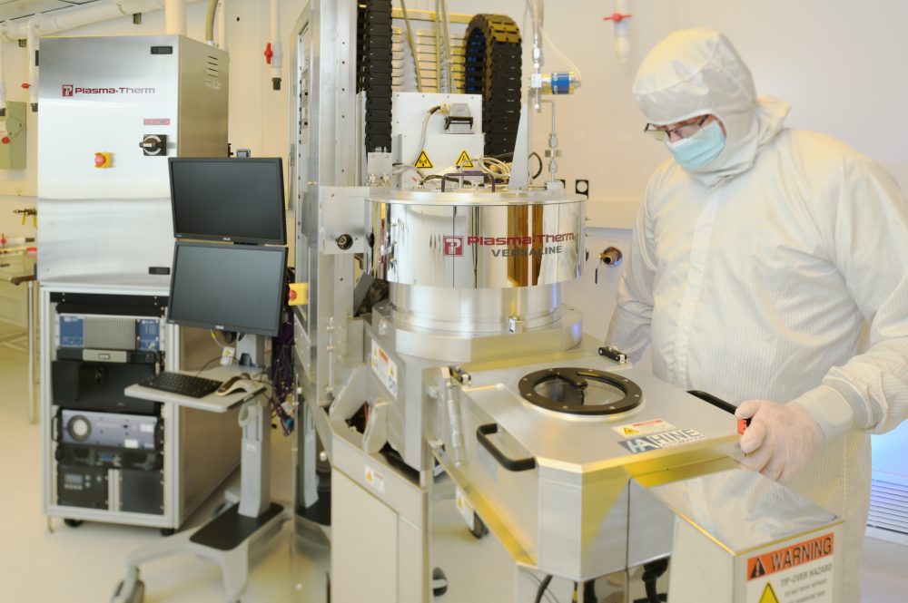 A physics students in a cleanroom suit works at equipment.