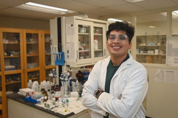 Dhairya Desai wears a lab coat and poses in the lab with equipment.